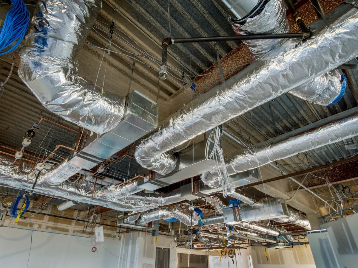 An industrial ceiling with metallic ductwork and piping, showcasing ongoing construction and HVAC installation.