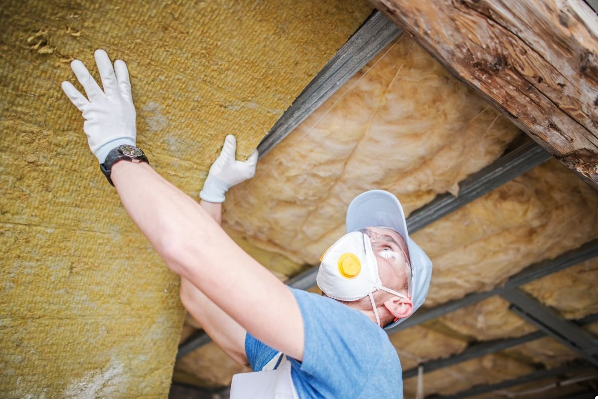 A man in a mask and gloves installs insulation, focusing on safety while working on a construction project.