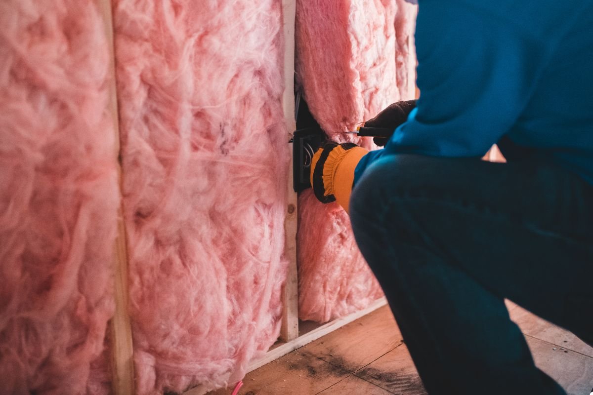 A man installs pink insulation in a wall, focused on his task in a construction setting.