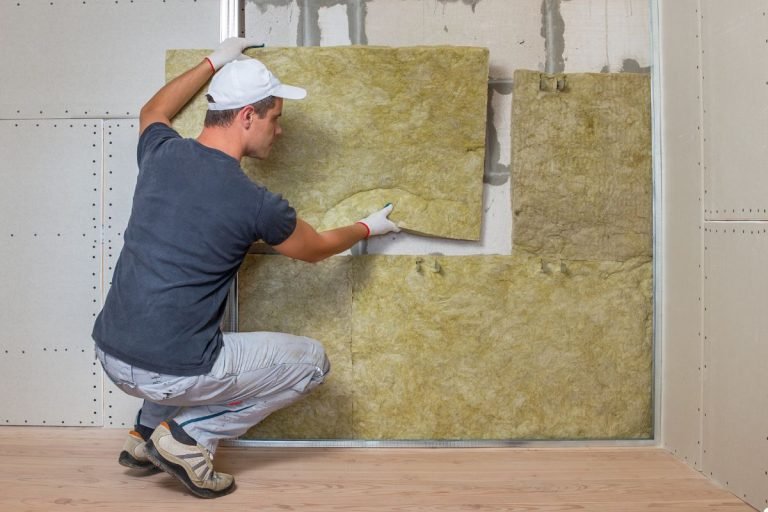 A man installs insulation in a room, carefully placing materials between the wall studs for energy efficiency.