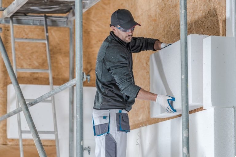 A man is engaged in wall work, using tools in a bright, organized room.