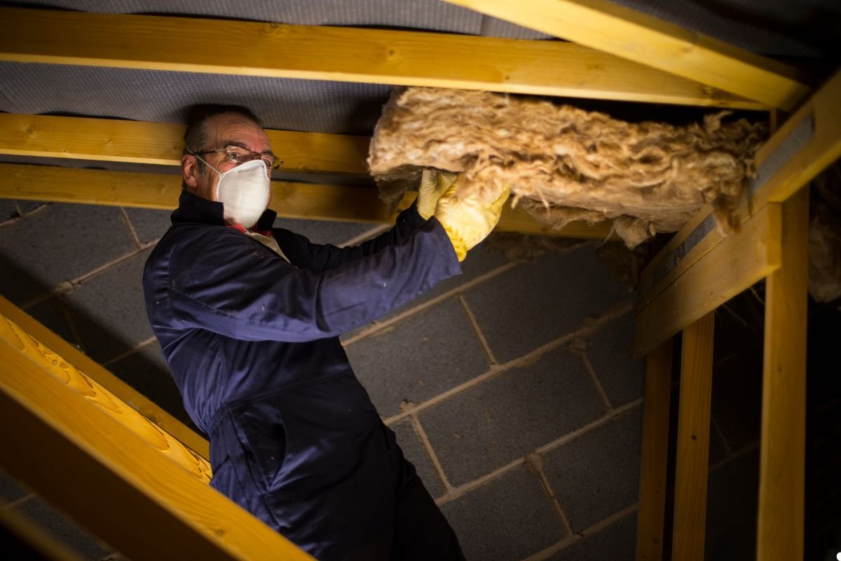 A man in a mask and gloves is repairing a roof, demonstrating safety precautions while working at height.
