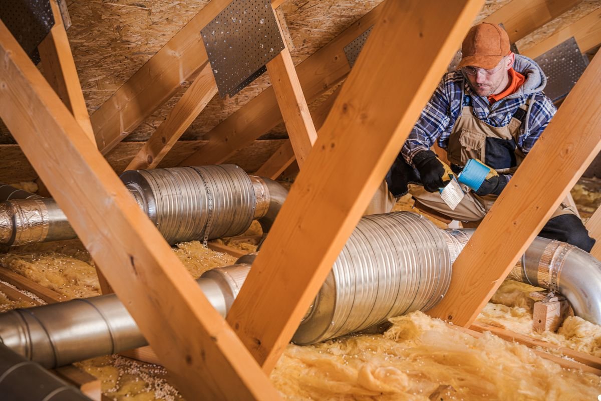 A man installing insulation on a roof, wearing safety gear and focused on his task under a clear blue sky.